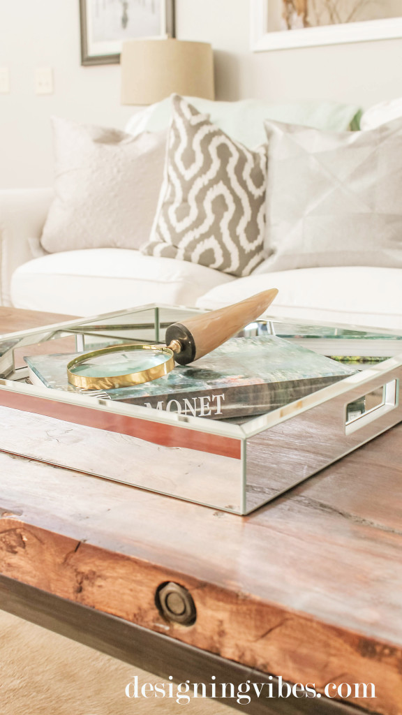 A wooden coffee table with a metal tray on top and a book and magnigying glass on it.