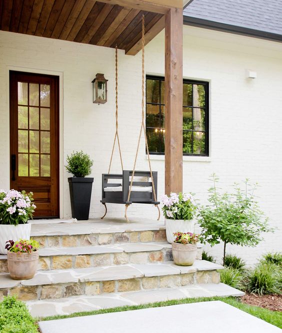 modern porch swing next to wooden front door of a white house