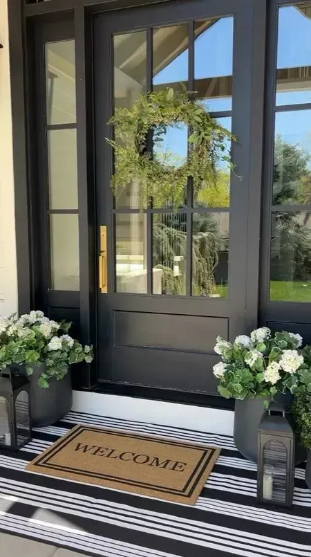 black front door with wreath and black lanterns and flowers beside it 