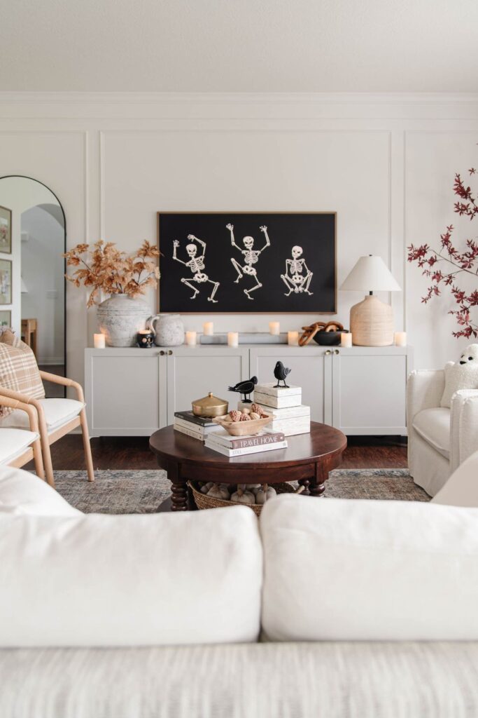 neutral living room decorated with chic halloween decor including candles, fall stems and skeleton frame tv art