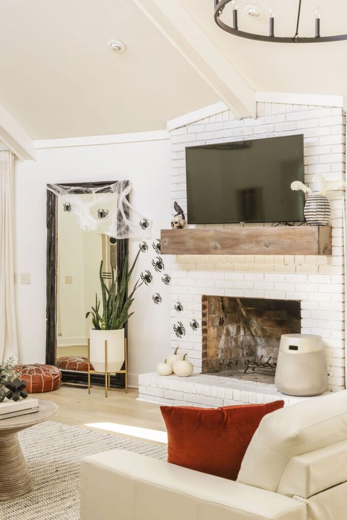 elegant living room decorated for halloween with spiders and spider webs on the mirror and white pumpkins on fireplace