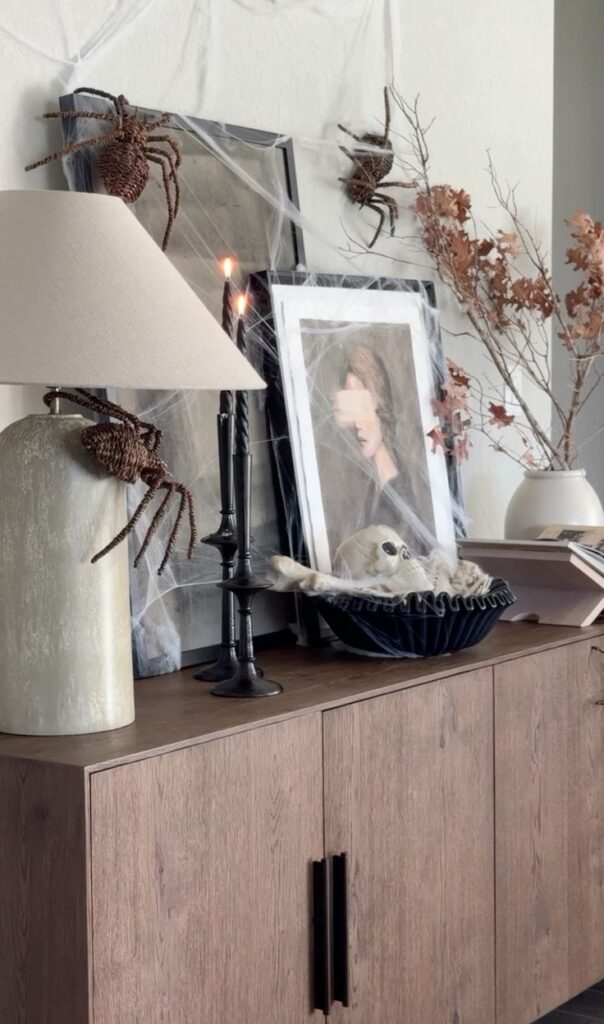 modern console table styled with elegant halloween decor including black candle sticks, spider webs and a decorative bowl of skeletons