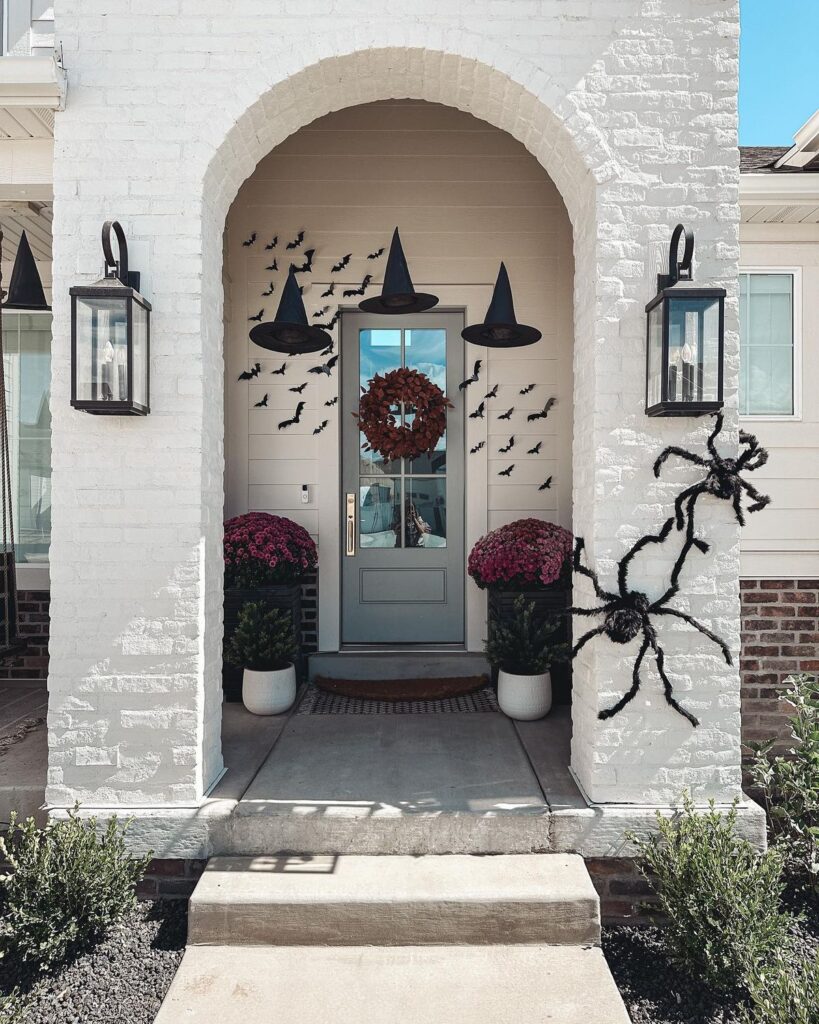 white home exterior decorated for halloween with large spiders, bats, mums and witches hats