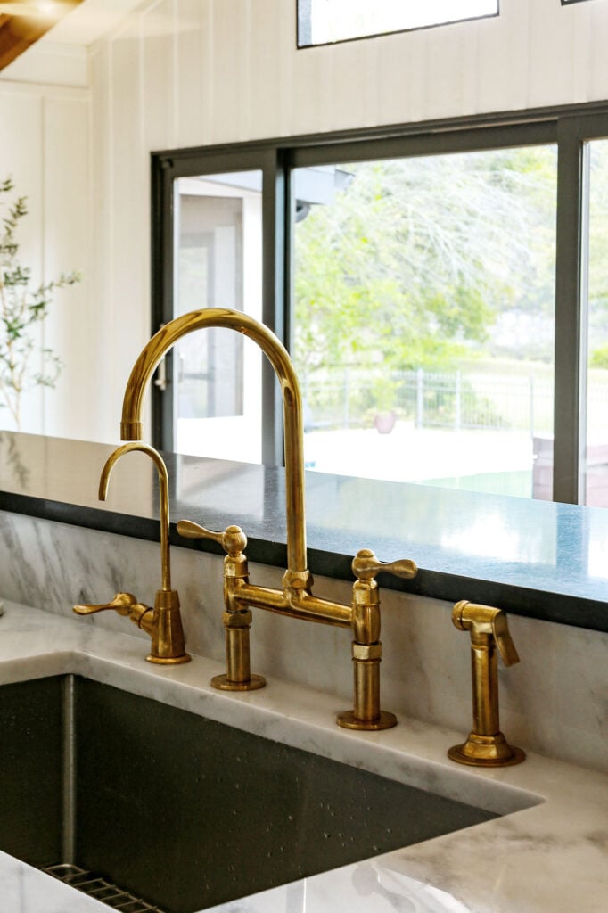 close up on a unlaquered brass bridge faucet sprayer combo in a kitchen with marble counters