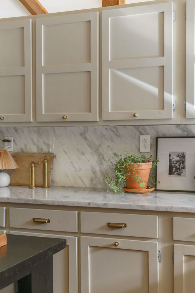 marble countertops and backsplash in kitchen with greige cabinets and brass hardware