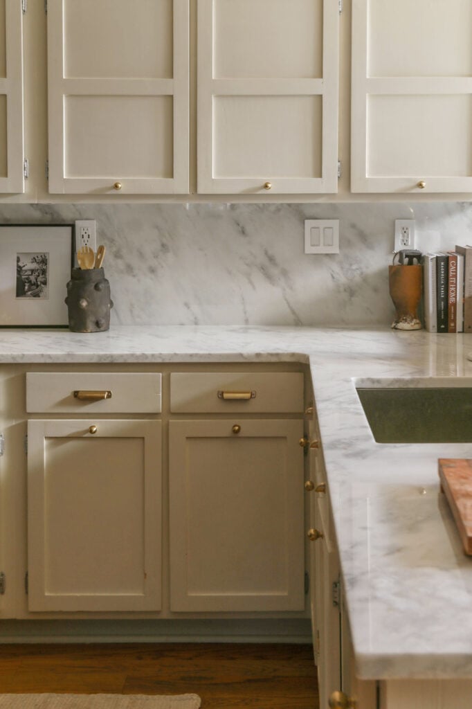 close up of polished marble countertops with backsplash and greige cabinetry in kitchen