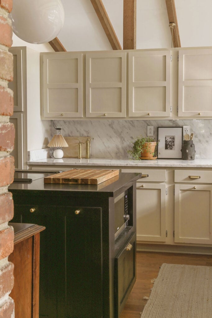moody kitchen with brick fireplace, black island and greige cabinets on the perimeter with polished marble backsplash and countertops