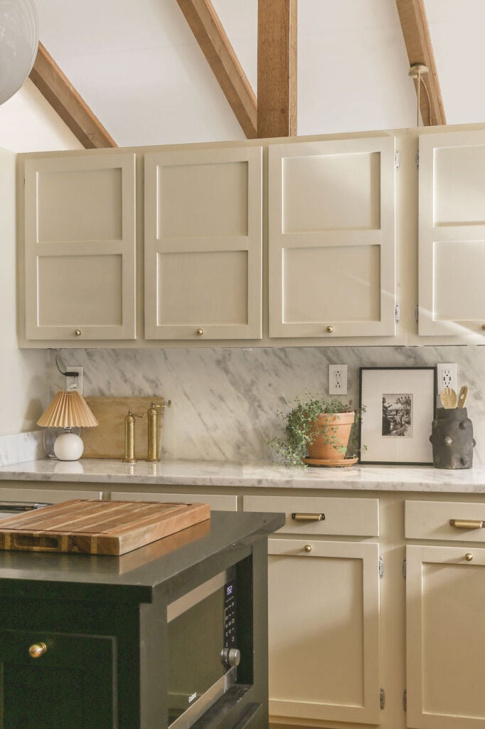 cottage kitchen with marble counters and backplash, greige cabinets and brass hardware