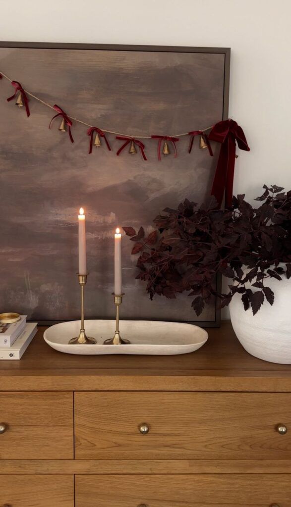 console table styled for christmas with bell garland with burgundy bows and burgundy floral arrangement