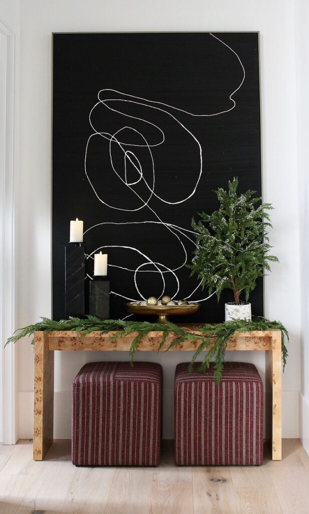 modern console styled for christmas with garland and burgundy ottoman stools