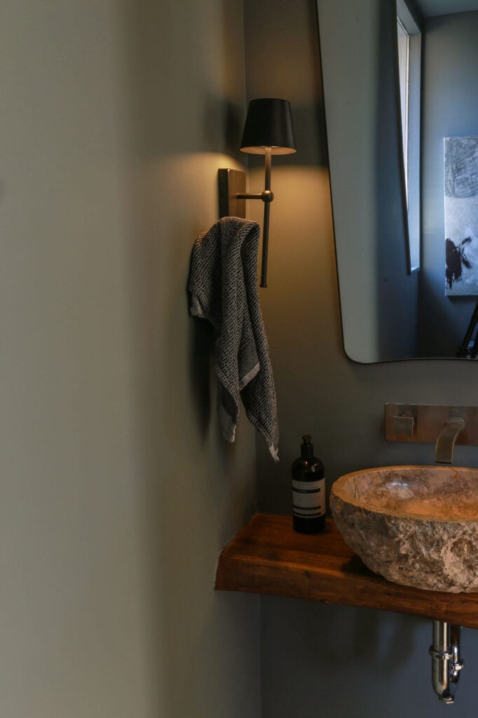moody powder room with black mirror and sconces and stone sink