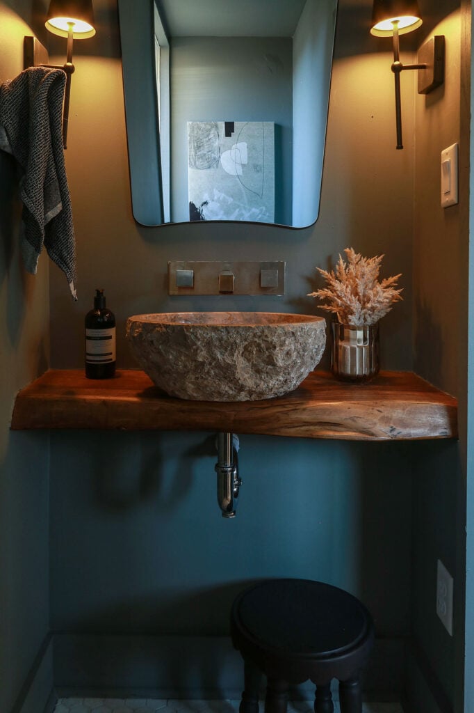 color drenched moody powder room with wood vanity and travertine sink