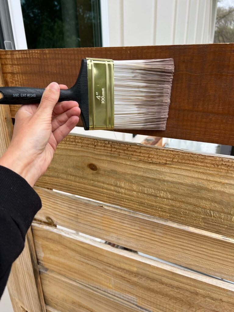 staining an outdoor diy fence with a brush and a rich chocolate color 