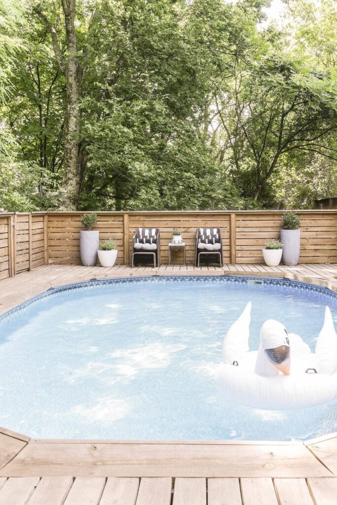 stylish above ground pool and deck with 2 arm chairs and table between 